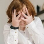 a boy in white polo covering his face with his hands