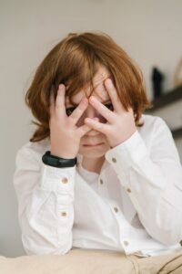 a boy in white polo covering his face with his hands